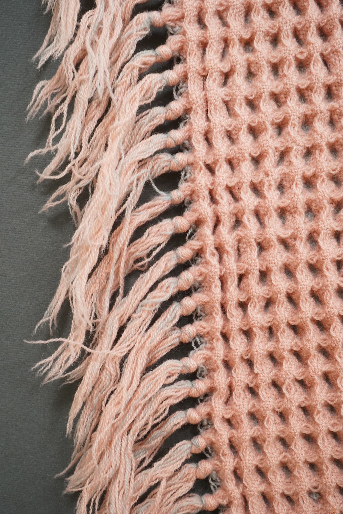 A pink and grey Welsh blanket with tasseled edges